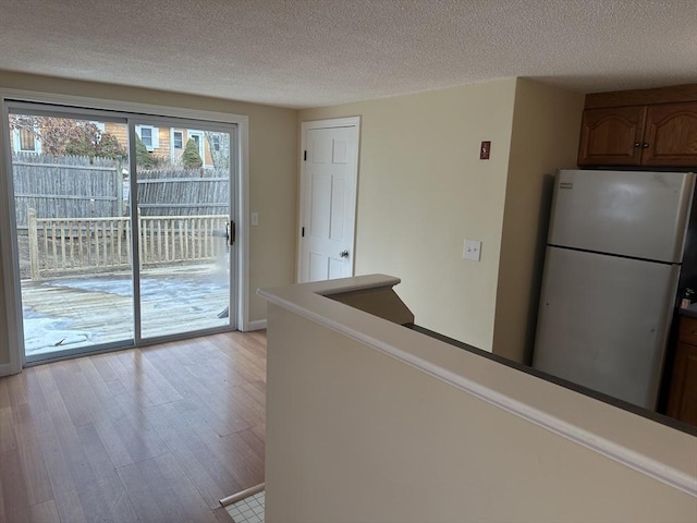 kitchen with a textured ceiling, light wood finished floors, brown cabinetry, and freestanding refrigerator