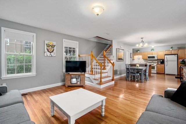 living room featuring stairway, a chandelier, baseboards, and light wood finished floors