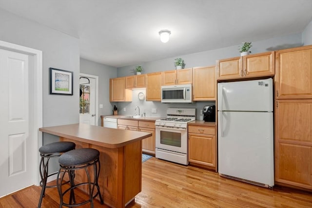 kitchen with white appliances, a sink, a breakfast bar area, light wood finished floors, and light brown cabinetry