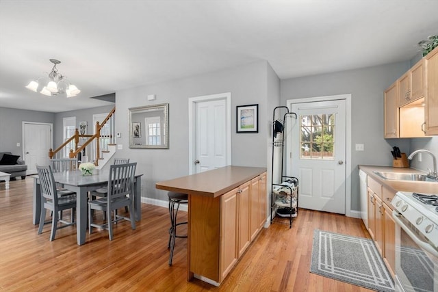 kitchen featuring a sink, white range with gas stovetop, a chandelier, light wood-style floors, and baseboards