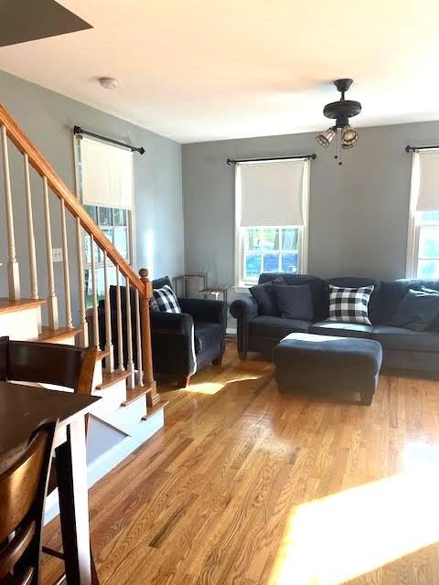 living area with stairs, wood finished floors, and a ceiling fan
