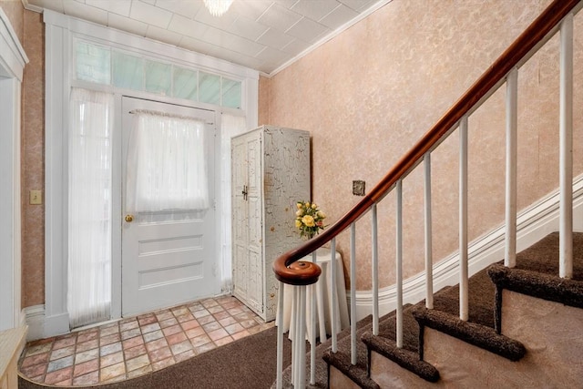 foyer entrance with stairs, carpet flooring, and crown molding