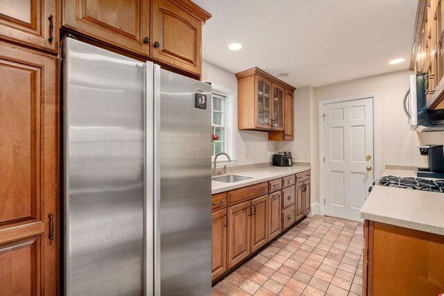 kitchen with appliances with stainless steel finishes, brown cabinets, a sink, light countertops, and glass insert cabinets
