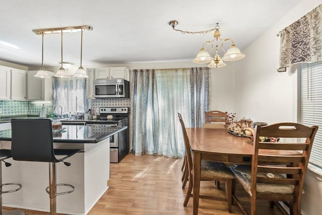 kitchen featuring light wood-style flooring, decorative backsplash, appliances with stainless steel finishes, dark countertops, and a chandelier