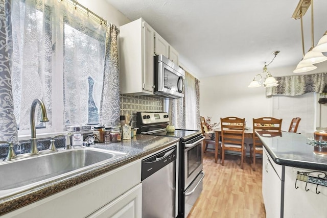 kitchen with a sink, decorative light fixtures, dark countertops, appliances with stainless steel finishes, and light wood finished floors