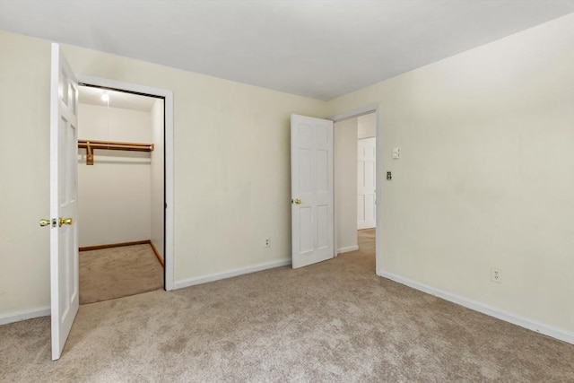 unfurnished bedroom with a walk in closet, light colored carpet, and baseboards