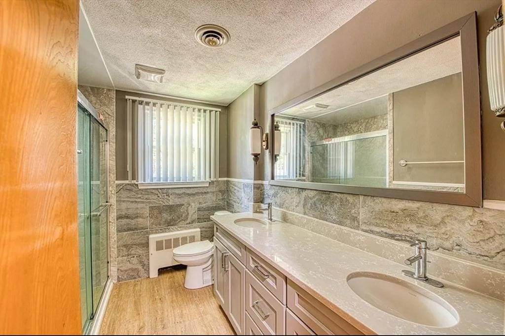 bathroom featuring tile walls, radiator, a sink, and a textured ceiling