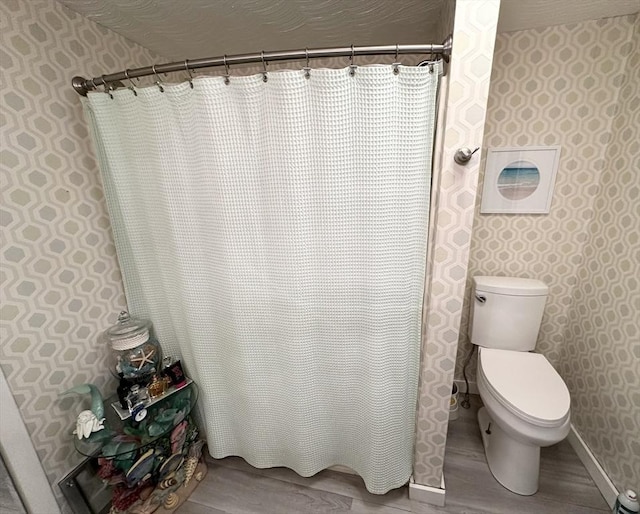 full bathroom with a shower with shower curtain, wood finished floors, baseboards, wallpapered walls, and toilet