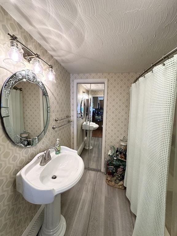 full bathroom with wallpapered walls, a shower with curtain, wood finished floors, and a textured ceiling