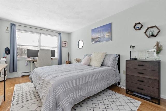 bedroom with a baseboard heating unit, baseboards, and light wood-style floors