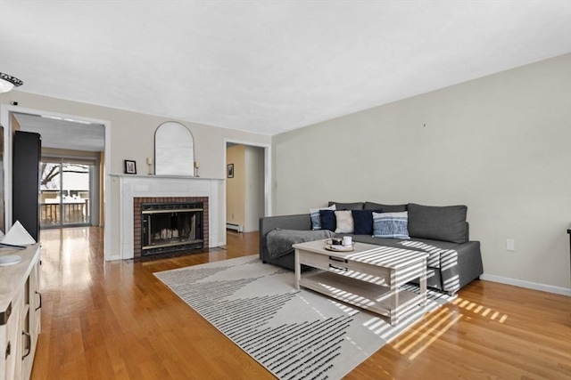 living room with a baseboard heating unit, baseboards, a brick fireplace, and light wood-style flooring