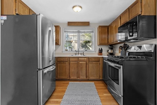 kitchen with light wood-style flooring, a sink, light countertops, appliances with stainless steel finishes, and brown cabinets