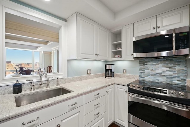 kitchen with appliances with stainless steel finishes, sink, white cabinets, backsplash, and light stone countertops