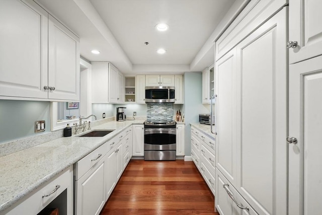 kitchen with sink, white cabinetry, dark hardwood / wood-style flooring, stainless steel appliances, and light stone countertops