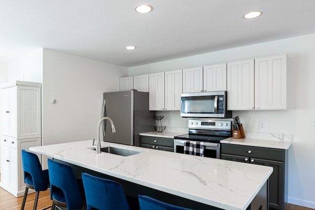 kitchen with a center island with sink, light hardwood / wood-style floors, light stone counters, and appliances with stainless steel finishes