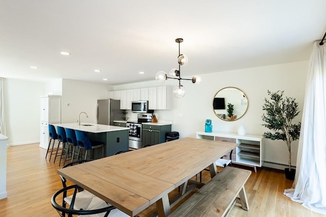 dining area with baseboard heating, sink, a chandelier, and light wood-type flooring