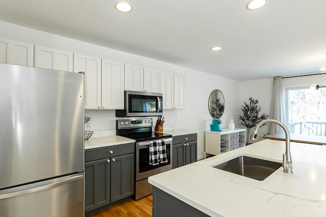 kitchen featuring appliances with stainless steel finishes, light stone counters, sink, light hardwood / wood-style flooring, and gray cabinets