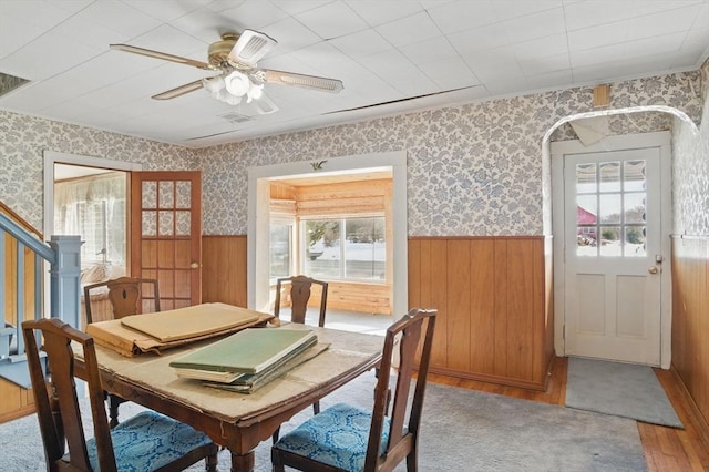 dining space with wallpapered walls, wood finished floors, and wainscoting