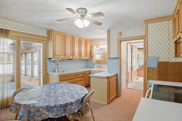 kitchen with wallpapered walls, light colored carpet, a wainscoted wall, light countertops, and light brown cabinets