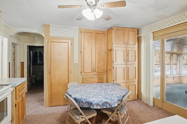 dining area featuring ceiling fan, a wainscoted wall, light colored carpet, and wallpapered walls