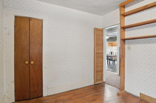 unfurnished bedroom featuring baseboards, hardwood / wood-style flooring, and wallpapered walls