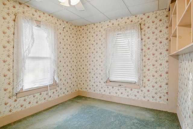 empty room featuring wallpapered walls, baseboards, a ceiling fan, a drop ceiling, and carpet flooring