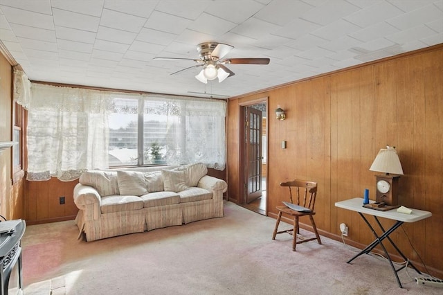 living area with wood walls, ceiling fan, and light colored carpet