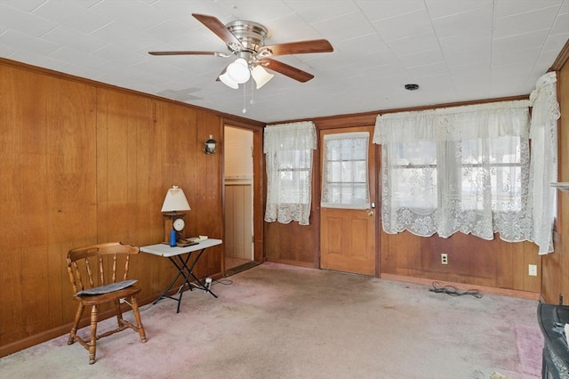 living area with a ceiling fan and wood walls