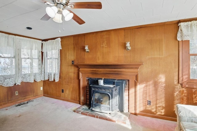 unfurnished living room featuring ceiling fan, wood walls, a wood stove, and light colored carpet