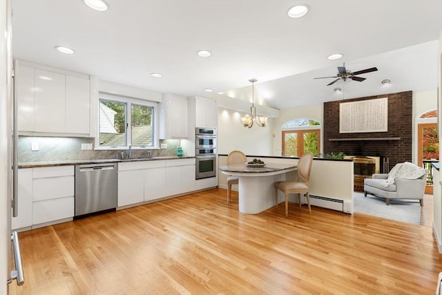 kitchen featuring appliances with stainless steel finishes, a breakfast bar, a sink, a brick fireplace, and white cabinetry