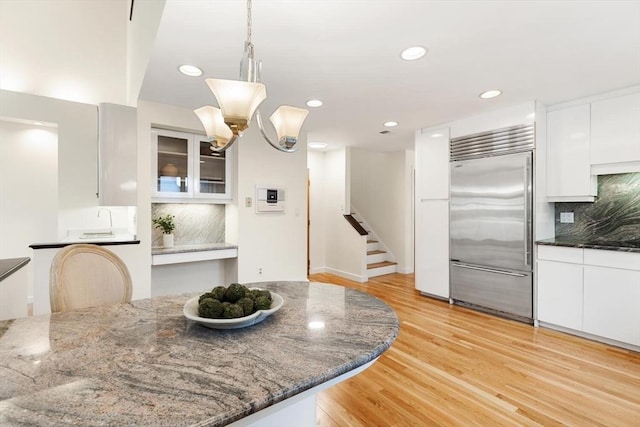kitchen with dark stone counters, decorative backsplash, stainless steel built in fridge, and white cabinets
