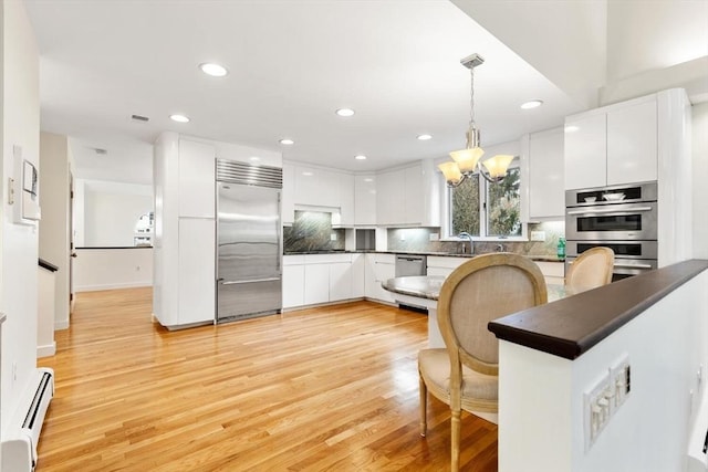 kitchen with pendant lighting, dark countertops, white cabinetry, a baseboard radiator, and appliances with stainless steel finishes