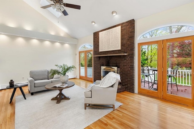 living area with french doors, light wood finished floors, a fireplace, and high vaulted ceiling