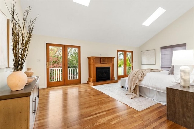 bedroom with access to exterior, a skylight, high vaulted ceiling, a glass covered fireplace, and light wood-style flooring