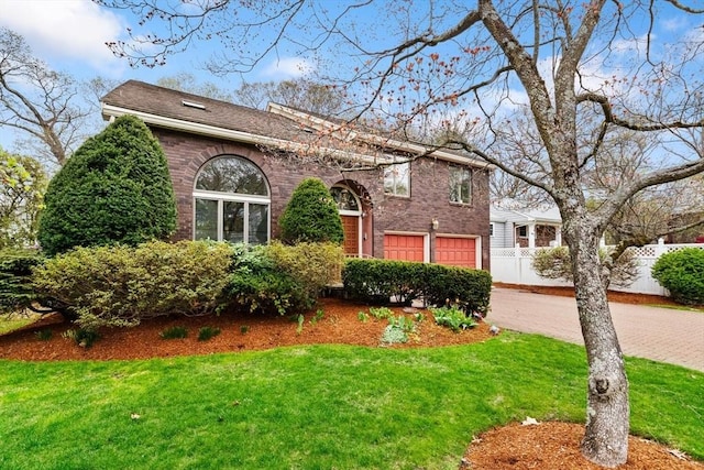 view of front facade featuring a front yard, a garage, brick siding, decorative driveway, and fence