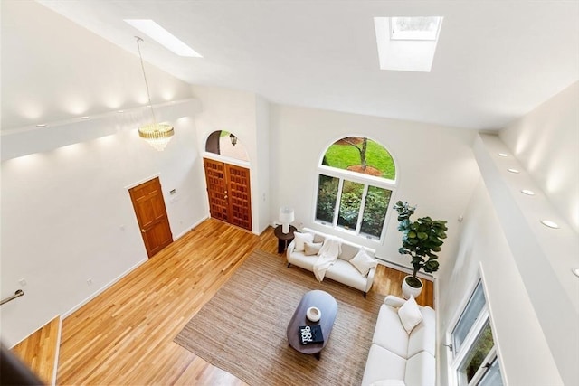 living room with a skylight, baseboards, high vaulted ceiling, and light wood-style floors