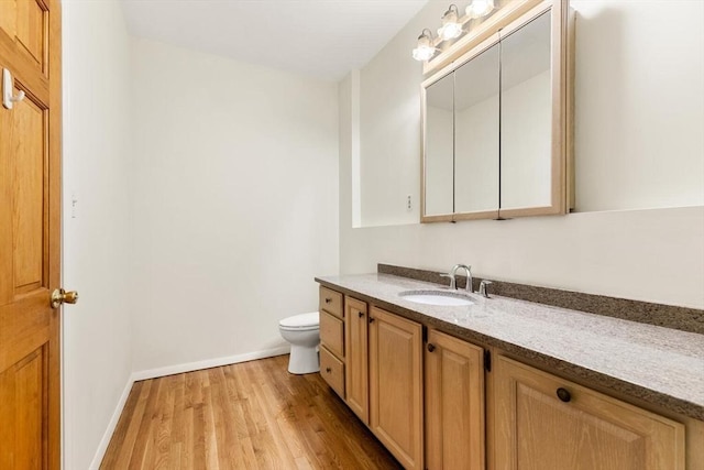 bathroom with vanity, baseboards, wood finished floors, and toilet