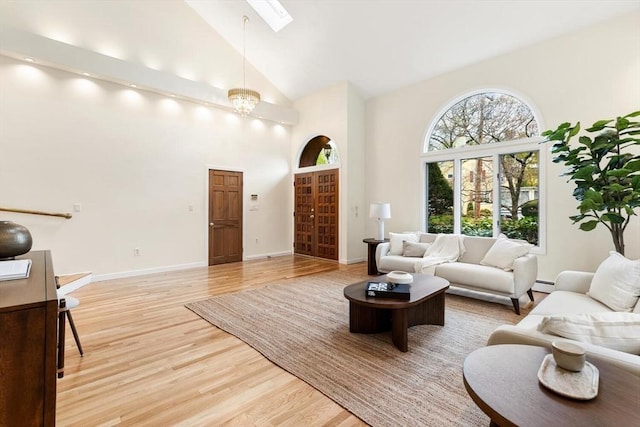 living room with a skylight, high vaulted ceiling, baseboards, a baseboard heating unit, and light wood-style floors