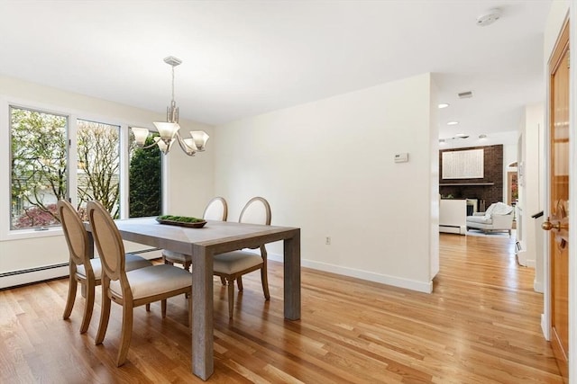 dining space featuring an inviting chandelier, light wood finished floors, baseboards, and a fireplace