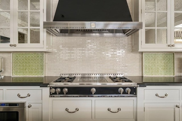 kitchen with cooktop, stainless steel oven, exhaust hood, dark countertops, and white cabinets