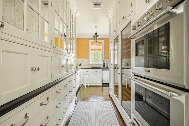 kitchen with a sink, stainless steel double oven, visible vents, white cabinets, and ornamental molding