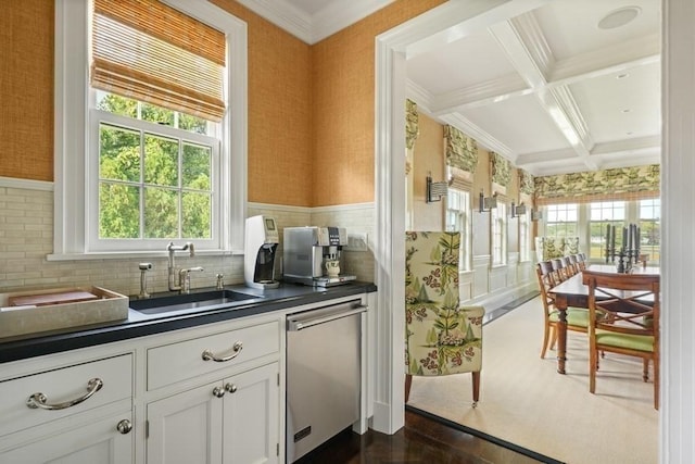 kitchen with wallpapered walls, a sink, dark countertops, and stainless steel dishwasher