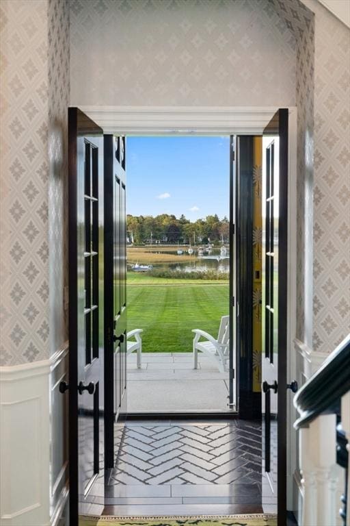 doorway to outside featuring wallpapered walls, hardwood / wood-style flooring, and wainscoting