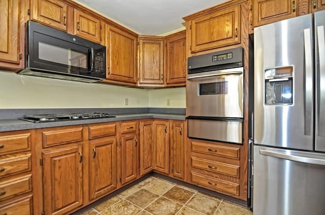 kitchen featuring appliances with stainless steel finishes, brown cabinetry, stone finish floor, and a warming drawer