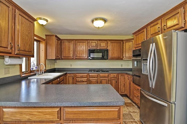 kitchen with a peninsula, brown cabinets, a sink, appliances with stainless steel finishes, and a warming drawer