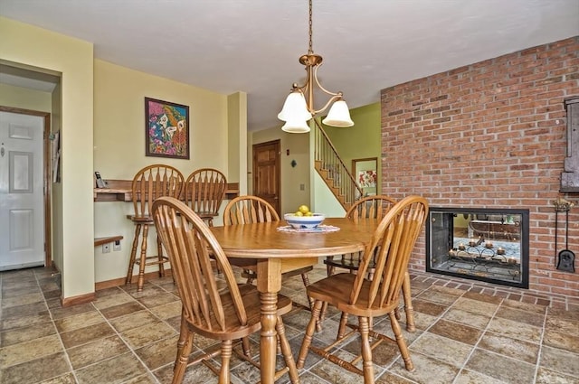dining area featuring an inviting chandelier, a brick fireplace, stairs, baseboards, and stone finish flooring