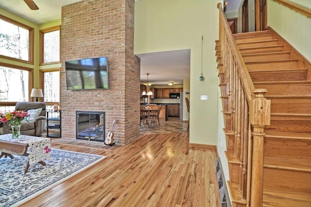 living room with a high ceiling, a fireplace, light wood-style floors, baseboards, and stairway