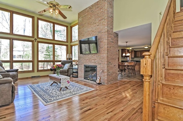living area featuring a brick fireplace, wood finished floors, a high ceiling, stairway, and a ceiling fan