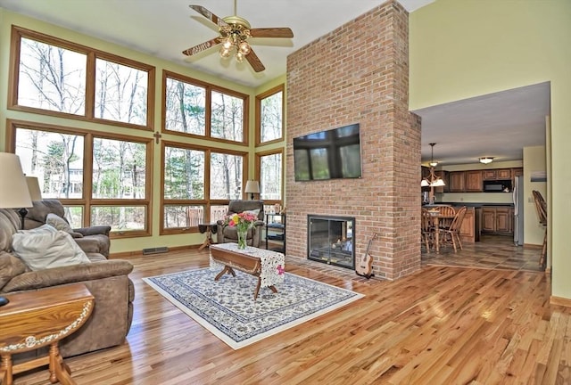 living room with a ceiling fan, a high ceiling, plenty of natural light, and light wood-style floors