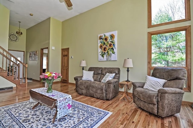 living area featuring wood finished floors, stairs, ceiling fan, and a high ceiling